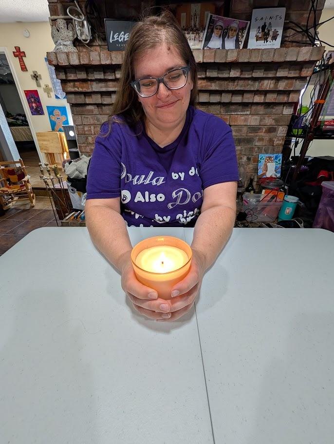 A woman sitting at a table holding a lit candle