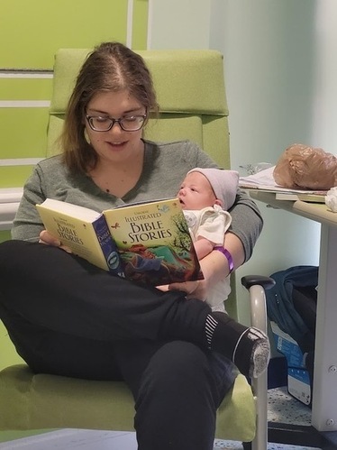 Doula Melanie Powell holding a newborn baby and reading a bible stories book. Doula Melanie Powell holding a newborn baby and reading a bible stories book.